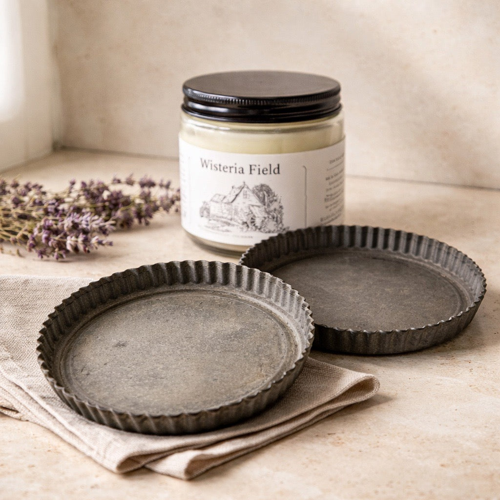Two ceramic tart tins on a cloth with a candle labeled 'Wisteria Field' in the background.