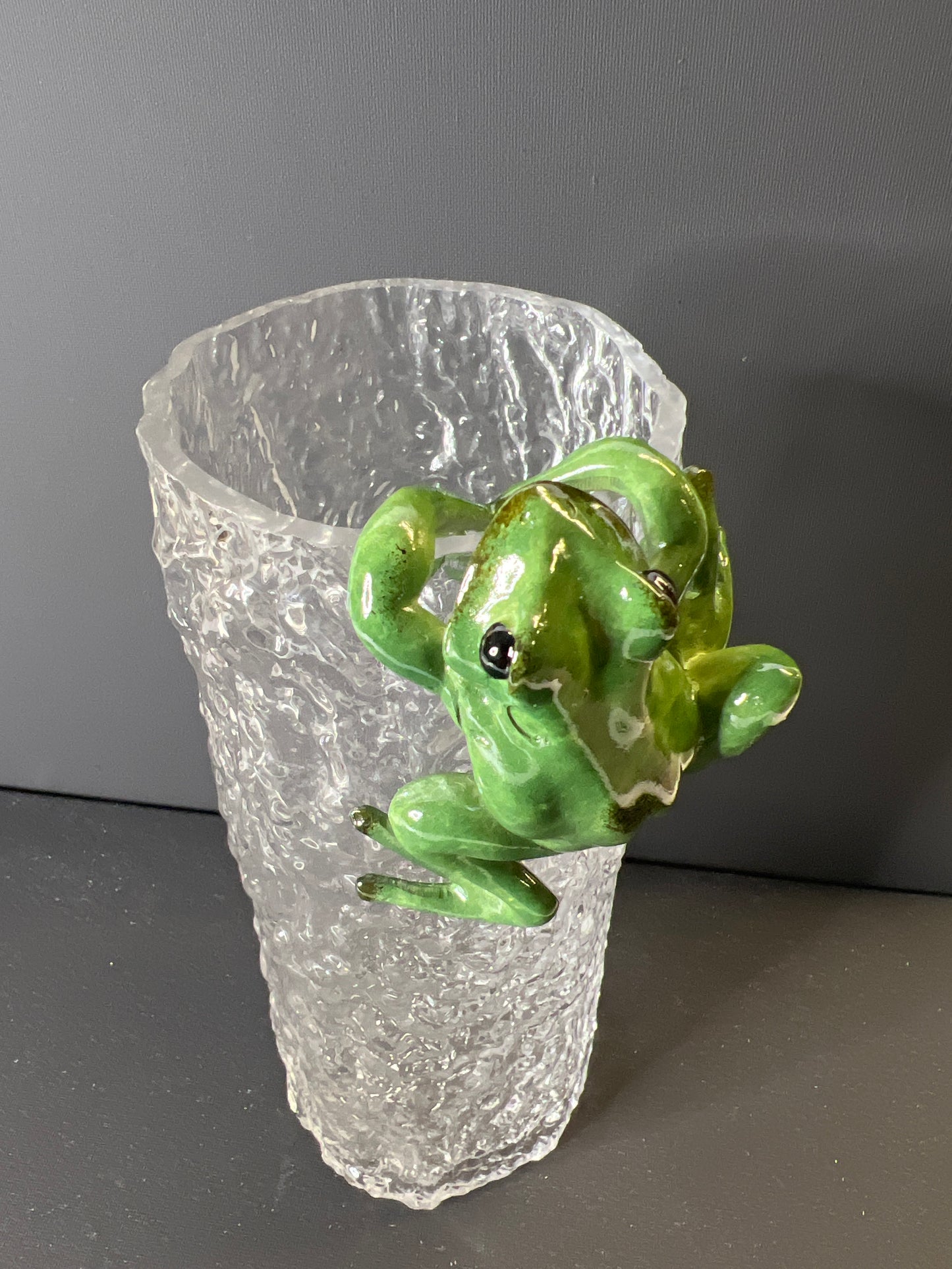 Green frog figurine on a clear crystal base against a dark background