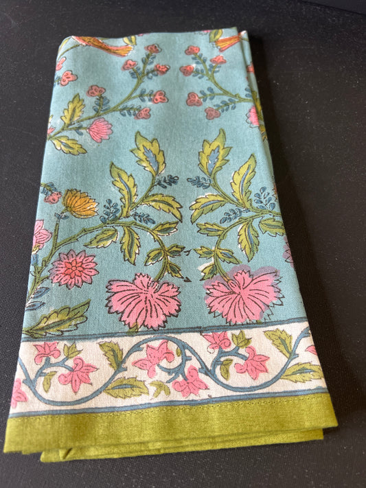 Floral patterned fabric with pink flowers and green leaves on a light blue background, folded and placed on a dark surface.