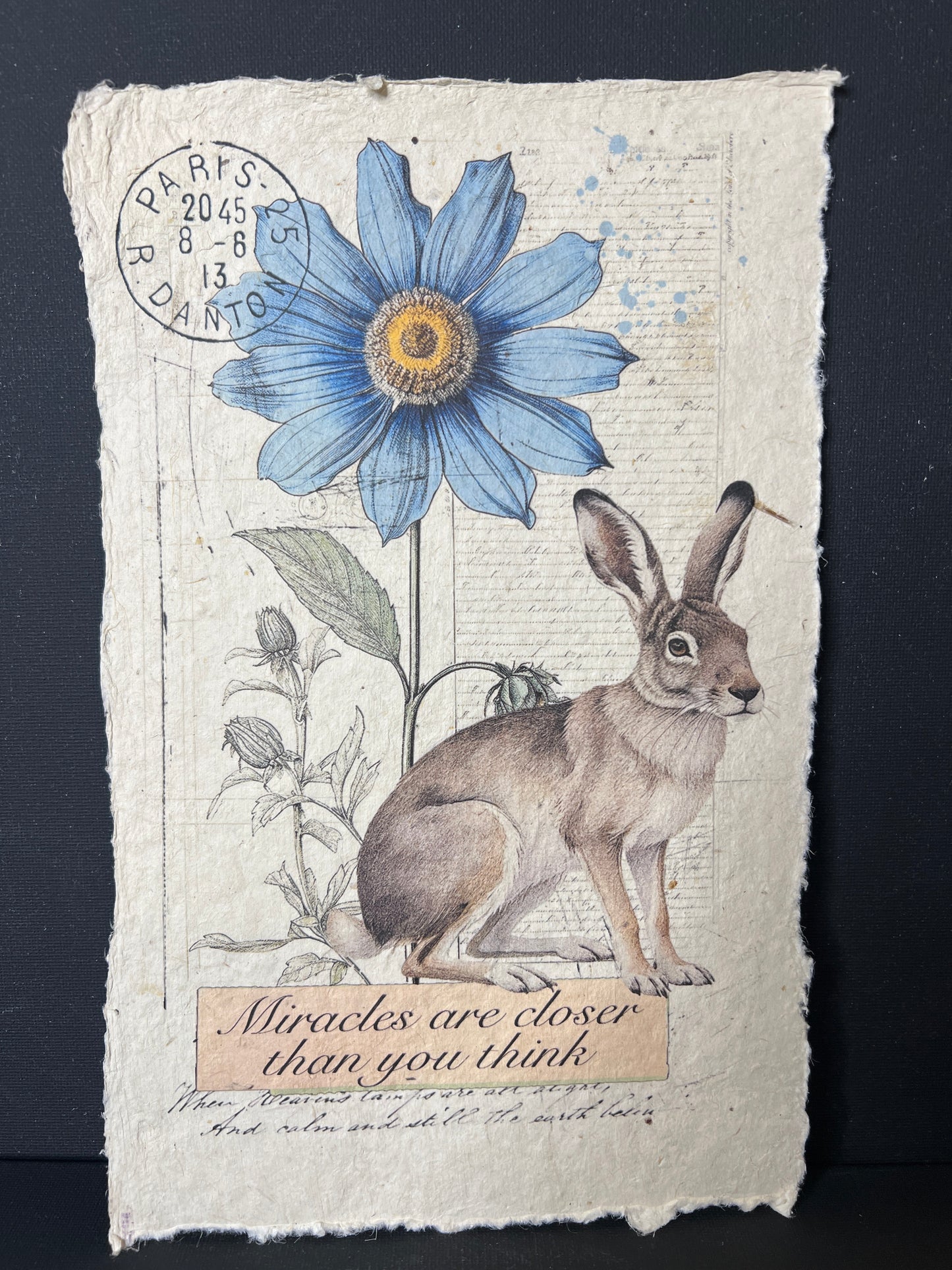 Vintage-style card with a rabbit and blue flower on textured paper.