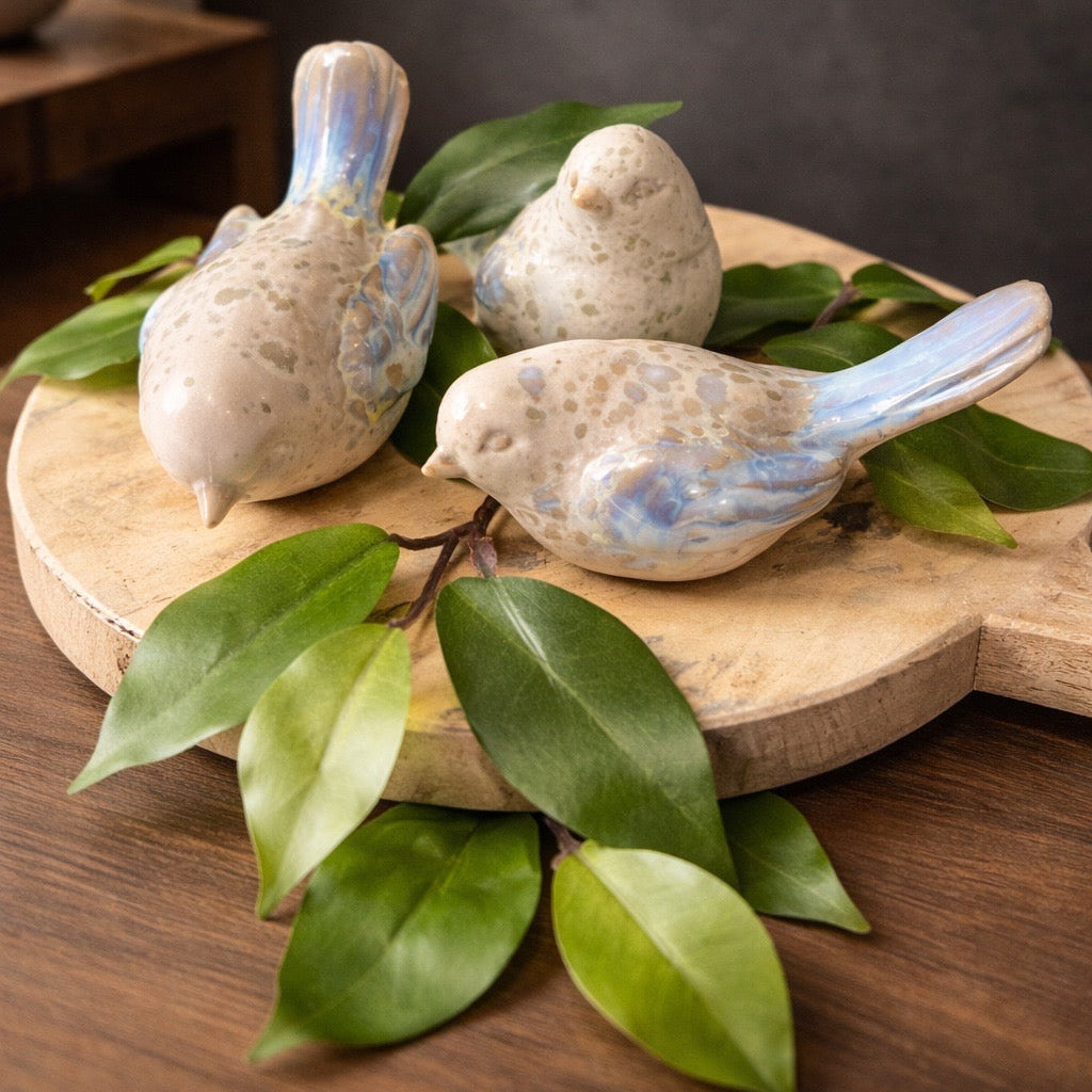 Three ceramic birds on a wooden board with leaves