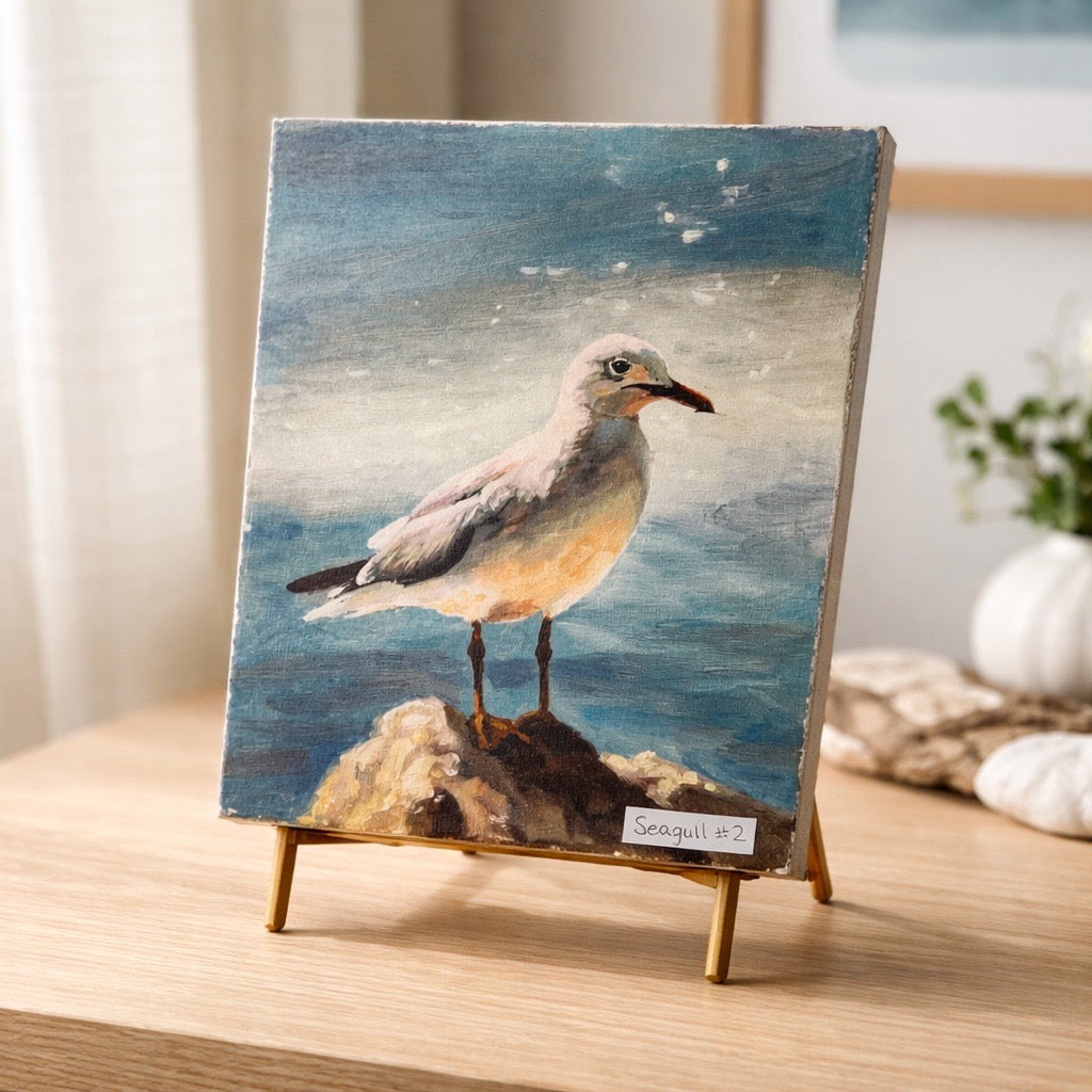 Small painting of a bird on a rock with a seascape background, displayed on a stand.
