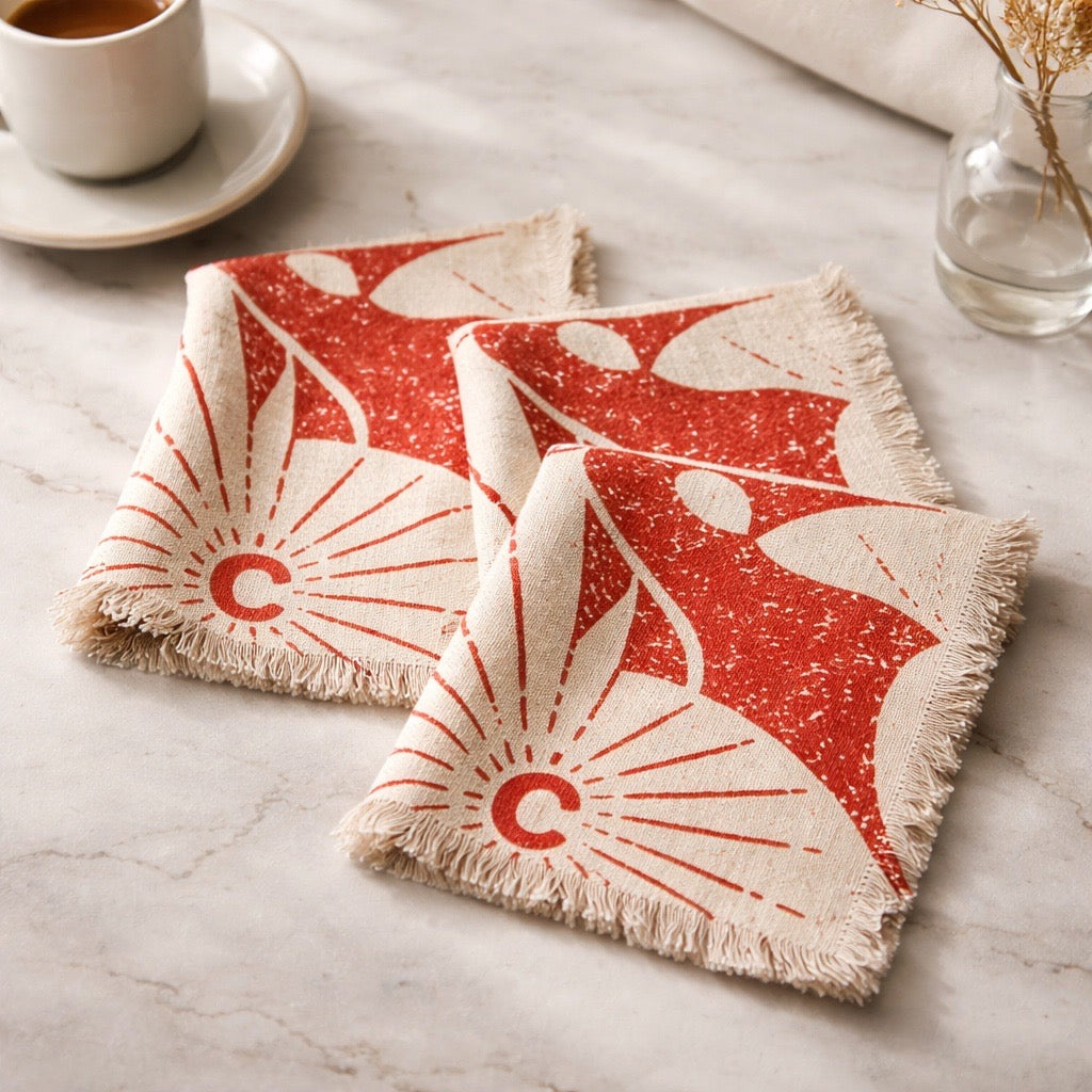 Two red and beige patterned coasters on a marble surface with a cup of coffee in the background.