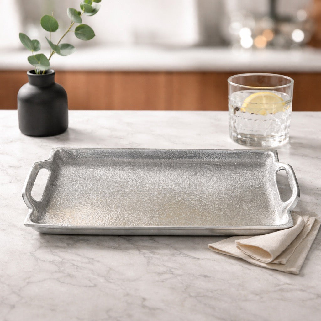 Silver tray on a marble countertop with a glass of water and a vase with greenery.